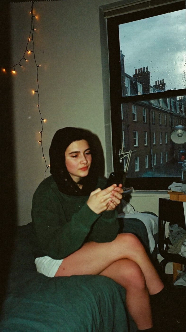 A young woman sitting on her bed at night, looking at her phone