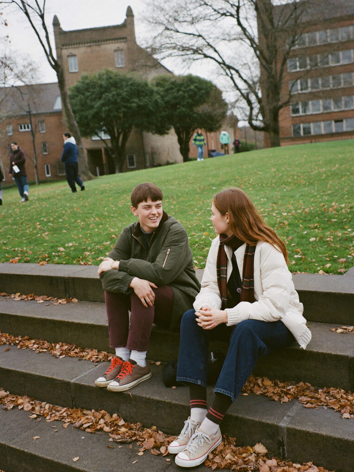 Two friends talking on stone steps on a college campus in autumn